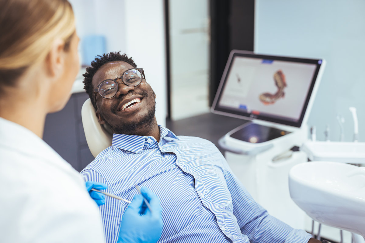 Close up portrait of smiling black man and dentist doctor hands holding tools. African American young man having a visit at the dentist's. He is sitting on chair at dentist office in dental clinic.